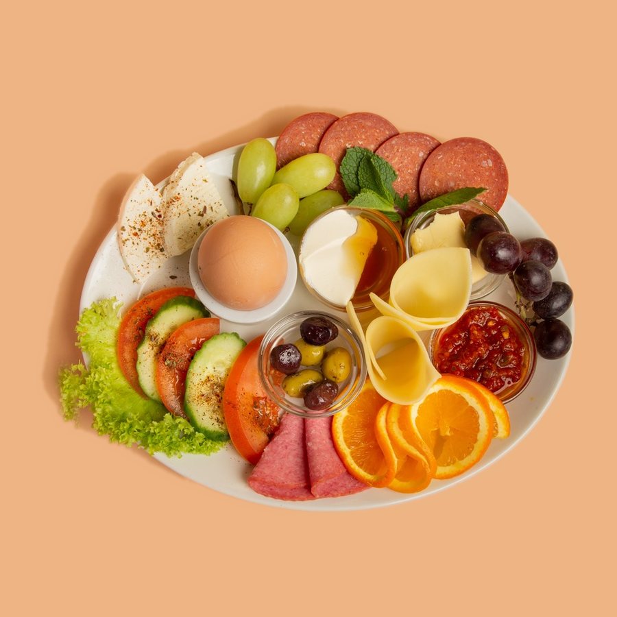 Frühstücksteller mit Käse, Wurst, Oliven, Ei und frischem Obst